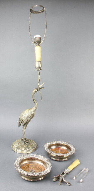 A pair of silver plated coasters, a ditto table lamp in the form of a heron, a ham holder and a pair of silver tongs 