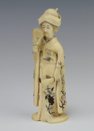 A Japanese carved ivory Meiji Okimono of a standing lady holding a fan and a flower with shibayama decoration to her gown 15cm 