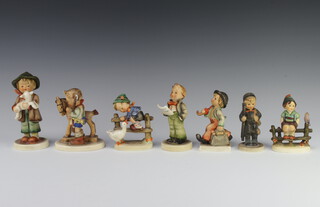 A Hummel figure of a boy holding a bag and an umbrella 10cm, a ditto of a girl with a wooden horse 12cm (stuck), ditto of a boy climbing a stile with a goose 10cm, a boy chimney sweep 10cm, a boy holding a hymn sheet 11cm (chipped), a boy holding a lamb 14cm (stuck) and a boy sitting on a stile 10cm (stuck)