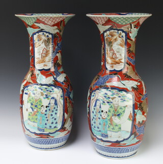 A pair of early 20th Century Arita porcelain baluster vases decorated with panels of figures in gardens on a ground of heron with flared necks 58cm 