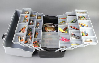 A collection of vintage fishing lures including Hardy, Abu, Mepps etc, contained in a black and grey plastic cantilever box 