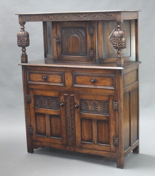 A carved oak court cupboard, the upper section enclosed by panelled doors and with 2 long drawers 138cm h x 109cm w x 45cm d  