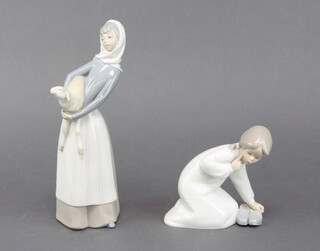 A Lladro figure of a young girl holding a pair of shoes 14cm and a ditto of a lady carrying a lamb 26cm 