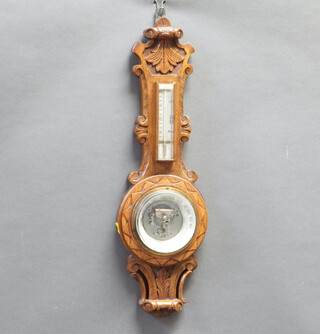 An aneroid barometer and thermometer contained in a carved oak wheel case, a section of timber missing to the top of the thermometer 