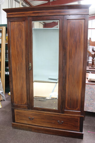 An Edwardian inlaid mahogany wardrobe with moulded cornice enclosed by a bevelled plate panelled mirrored door, the base fitted a drawer, raised on a platform base 204cm h x 132cm w x 55cm d (cornice damaged to 1 end, sun bleaching in places)