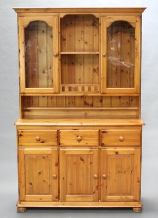 A pine dresser with moulded cornice, the raised back fitted a recess flanked by cupboards enclosed by glazed panelled doors, the base fitted 3 drawers above triple cupboard, raised on a platform base 186cm h x 117cm w x 43cm d  