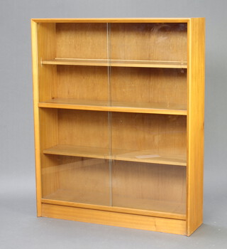 A 1950's light oak bookcase/display cabinet enclosed by glazed sliding panelled doors, raised on a platform base 112cm h x 91cm w x 24cm d 