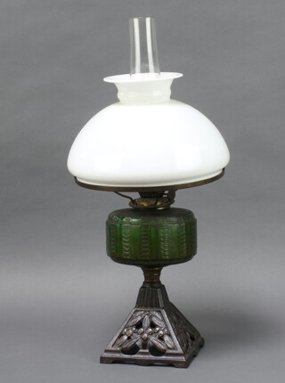 A Victorian green glass oil lamp reservoir raised on a pierced iron base with opaque shaped glass chimney 53cm x 15cm 