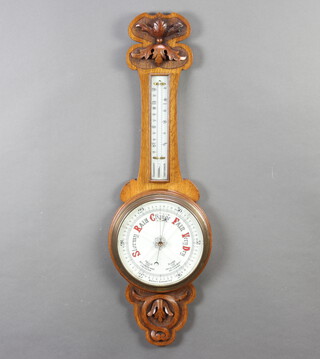 An Edwardian aneroid barometer and thermometer with porcelain dial, contained in a carved oak wheel case