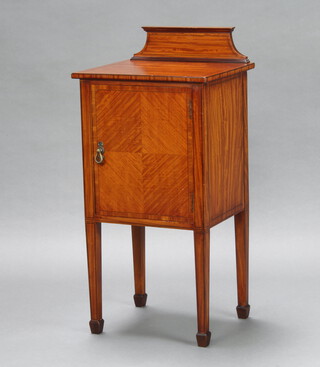An Edwardian Sheraton style satinwood bedside cabinet with raised back and cupboard enclosed by panelled door, raised on square tapered supports, spade feet 67cm h x 41cm w x 35cm d 