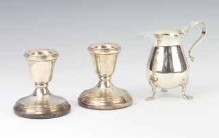 An Edwardian silver cream jug with paw feet Birmingham 1902, 6cm, 50 grams and a pair of dwarf silver candlesticks Birmingham 1986 5cm