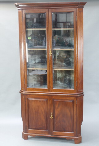 An Edwardian mahogany double corner cabinet with moulded cornice and fluted columns to the sides, fitted shelves enclosed by bevelled plate glazed panelled door, the base enclosed by a panelled door, raised on bracket feet 210cm h x 106cm w x 77cm d 