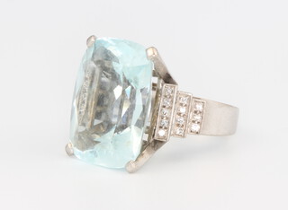 A white metal stamped 18k cushion cut aquamarine and diamond ring, the centre stone 21mm x 17mm x 11mm, flanked by 12 brilliant cut diamonds each 0.01ct, 17.7 grams, size L 1/2, stamped Kevin, together with original import tax certificate dated 1970 