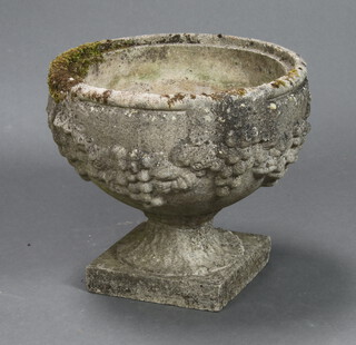 A circular well weathered reconstituted stone urn with swag and grape decoration, raised on a square base 39cm h x 42cm diam.  