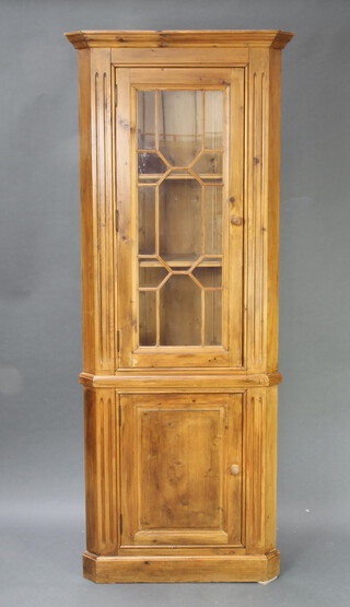 A Georgian style pine double corner cabinet with moulded cornice, fitted shelves enclosed by astragal glazed panelled door, the base enclosed by a panelled door with fluted columns to the side 186cm h x 79cm w x 50cm d 