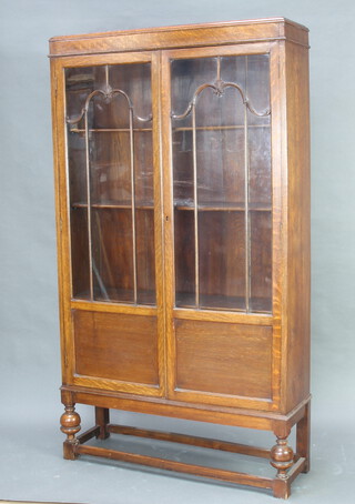 A 1930's oak bookcase fitted adjustable shelves enclosed by astragal glazed doors, raised on cup and cover supports 176cm x 100cm x 30cm (escutcheon missing, split to back
