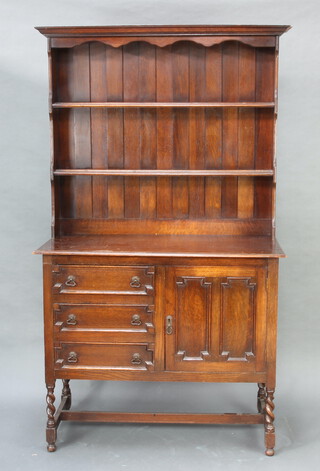 A 1930's Jacobean style oak dresser, the raised back with moulded cornice, fitted three shelves above three long drawers, flanked by cupboard and raised on spiral turned supports with H framed stretcher 186cm h x 107cm w x 49cm d (ring and water marks to the top)
