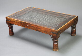 A rectangular Indian carved hardwood coffee table, the centre inset a window panel with wrought iron trellis work and glass top, raised on turned supports 40cm h x 119cm l x 75cm w