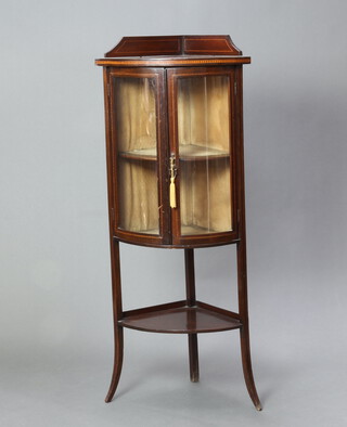 An Edwardian inlaid mahogany bow front corner cabinet with raised back, fitted shelves enclosed by glazed panelled doors, raised outswept supports with undertier 129cm h x 54cm w x 38cm d 