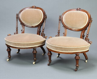A pair of Victorian walnut show frame nursing chairs with fluted columns to the sides, seats and backs upholstered in mushroom material, raised on turned and fluted supports with ceramic casters 77cm h x 64cm w x 50cm d (seat 39cm x 30cm) 