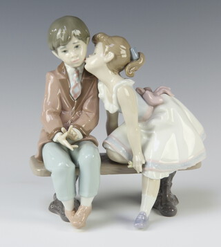 A Lladro group of a young couple sitting on a bench kissing 7635 19cm 