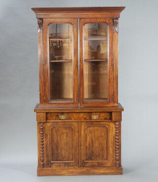 A Victorian mahogany display cabinet on cabinet, the upper section with moulded cornice, fitted shelves enclosed by a pair of arched panelled glazed doors, the base fitted a drawer above cupboard enclosed by a pair of arched panelled doors, with columns to the sides 201cm h x 104cm w x 38cm d 