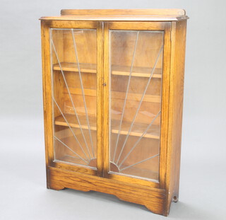 An Art Deco oak display cabinet with raised back, fitted shelves enclosed by a lead glazed sunburst panel door, on a platform base 125cm h x 91cm w x 26cm d 