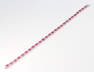 An 18ct white gold oval ruby and diamond line bracelet, the rubies 12.23ct, the diamonds 0.55ct, 18cm, 9.1 grams 