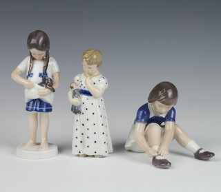 A Royal Copenhagen figure of a standing girl 427 16cm, a ditto of a girl holding a doll 3539 14cm and a Bing & Grondahl figure of a girl tying her shoes 11cm 