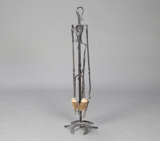 A blacksmiths wrought iron made 4 piece fireside companion set with poker, tongs, shovel and brush, raised on a stand with horseshoe base  94cm h x 26cm 