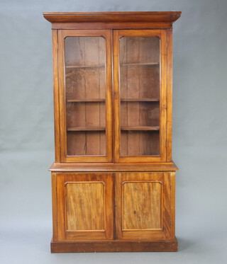 A Victorian mahogany bookcase on cabinet, the upper section with moulded cornice, fitted shelves enclosed by glazed panelled doors, the base enclosed by a pair of oval panelled doors, raised on a platform base 215cm h x 117cm w x 43cm d 