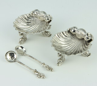 A pair of Victorian style cast silver table salts in the form of shells, raised on dolphin feet with 2 similar spoons, rubbed marks, 110 grams 