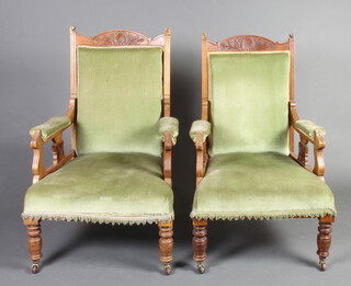 A pair of Edwardian carved walnut show frame open arm chairs, the seats and backs upholstered in green material, raised on turned supports 100cm h x 67cm w x 65cm d (seat 42cm x 38cm) 