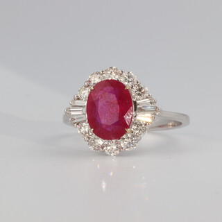 An 18ct white gold oval ruby and diamond cluster ring, the centre stone 2.05ct, the tapered baguettes and brilliant cut diamonds 0.85ct, 3.8 grams, size N 1/2