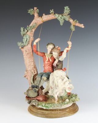 A late Capodimonte group of 2 figures on a swing, raised on a wooden socle 43cm 