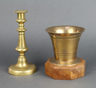 A 17th/18th Century brass mortar 10cm x 13cm, raised on an octagonal wooden base together with an 18th Century brass candlestick with ejector 21cm x 10cm (some dents) 