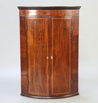 A Georgian inlaid mahogany bow front hanging corner cabinet with moulded cornice, fitted shelves enclosed by a pair of panelled doors with ivory diamond shaped escutcheons 100cm h x 68cm w x 46cm d  