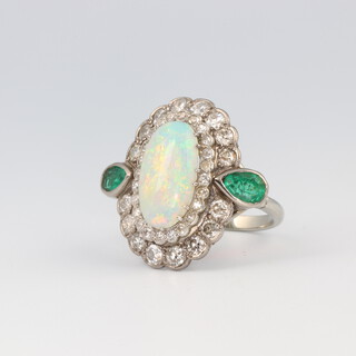 A fine white metal oval opal, diamond and emerald cocktail ring, the centre oval opal 16mm x 7mm, the 16 brilliant cut diamonds each 0.05ct, the 24 smaller diamonds each 0.01ct and the 2 pear cut emeralds each 0.25ct (both chipped) 8.7 grams, size O 