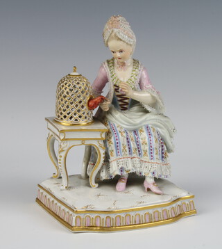 A 19th Century Meissen figure of a seated lady feeding a bird in a bird cage, raised on a rococo table 14cm 