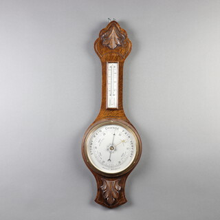 A 1930's aneroid barometer and thermometer with silvered dial contained in a carved oak wheel case 75cm h x 22cm w x 3cm d 
