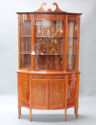 An Edwardian heavily inlaid throughout mahogany bow front display cabinet, the upper section with broken pediment and fitted shelves, the base fitted a drawer above panelled doors, raised on square tapered supports with spade feet 223cm h x 123cm w x 