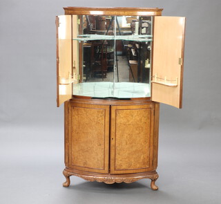 A 1930's bleached figured walnut bow front corner cocktail cabinet, the upper section with mirrored back enclosed by a panelled door, the base fitted a cupboard enclosed by a panelled door, raised on cabriole supports 156cm h x 82cm w x 52cm d 
