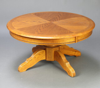 An American style circular oak finished coffee table with quarter veneered top, raised on a turned column and tripod base 46cm h x 91cm diam. 
