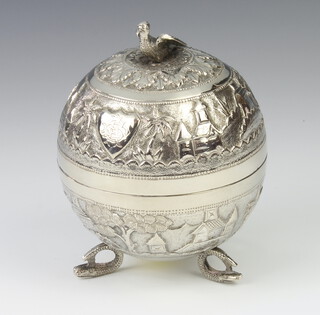 An Indian repousse silver circular box with bird finial decorated with buildings, engraved with monogram, raised on dolphin feet, 12cm, 190 grams