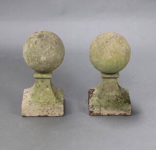 A pair of well weathered reconstituted stone circular garden gate post caps, raised on square outswept bases 44cm h x 23cm x 23cm 