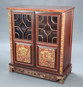 A Chinese carved hardwood cabinet, fitted shelves enclosed by a pair of astragal glazed panelled doors, raised on carved and pierced supports 118cm h x 102cm w x 49cm d 