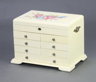 A white and floral painted jewellery chest with hinged lid revealing a plush lined interior, the base fitted 6 short and 1 long drawers, having carrying handles to the sides, raised on bracket feet 27cm h x 40cm w x 25cm d 