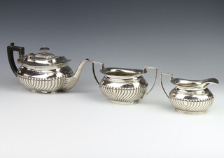 A matched silver 3 piece tea set with demi-fluted decoration and ebony mounts, the teapot Birmingham 1894, the milk jug Birmingham 1919 and the sugar bowl 1912, gross weight of 1016 grams  