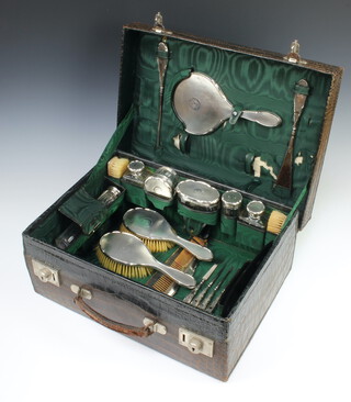 An Edwardian crocodile vanity case monogrammed GCD containing 6 silver lidded jars, 2 clothes brushes, a hand mirror, button hook, shoe horn, 2 hair brushes, a comb, 4 manicure implements, engraved with a monogram, Birmingham 1914 