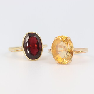A yellow metal stamped 18k citrine ring, 6.8 grams, size M together with a garnet ditto 4.6 grams size M 